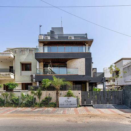 Modern multi-story residence with glass walls, wooden accents, and tropical landscaping.