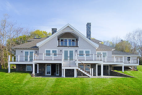 A large gray shingle-style house with a steep roof, dormers, and wraparound decks.