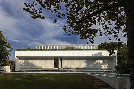 A modern, minimalist two-story house with large windows, a pool, and a lush green landscape.