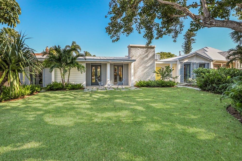 A well-maintained tropical home with a lush yard, palm trees, and a chic, modern exterior.