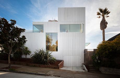 Modern white building with large windows and a palm tree in the foreground.