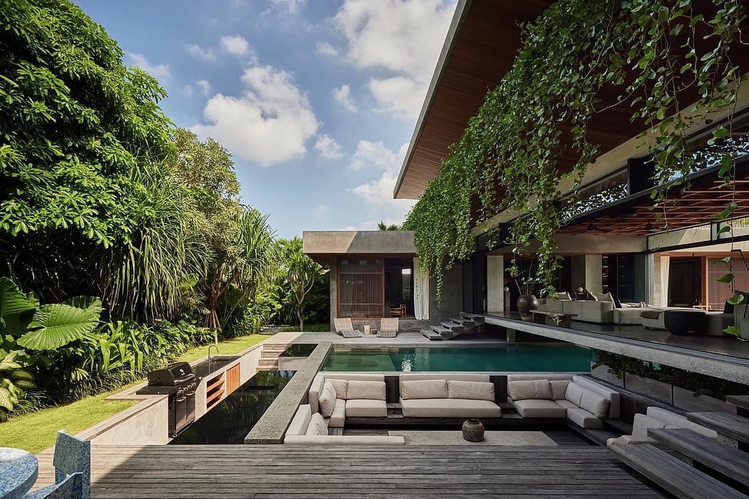 Lush tropical garden surrounds modern pool house with expansive wooden deck and seating area.