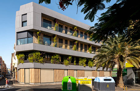 A modern, multi-story building with extensive greenery and balconies, situated in an urban setting.