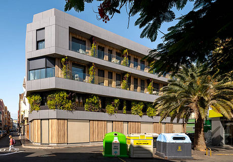 A modern, multi-story building with extensive greenery and balconies, situated in an urban setting.