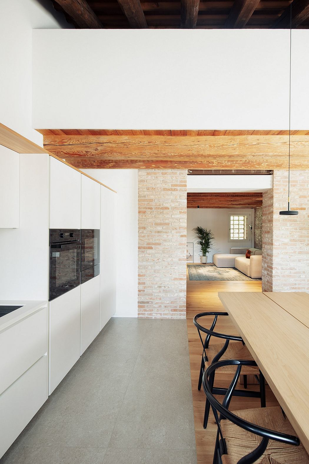 Warm wooden beams, exposed brick walls, and sleek white cabinetry create a modern yet cozy kitchen.