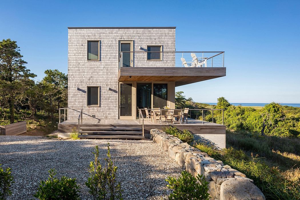 Modern coastal home with wood siding, balcony, and stone path leading to porch.