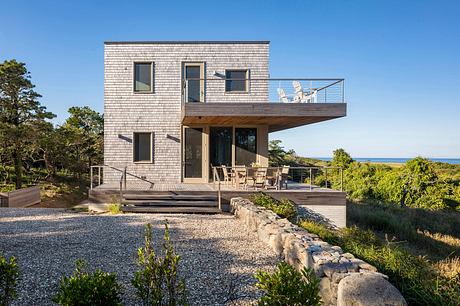 Modern coastal home with wood siding, balcony, and stone path leading to porch.