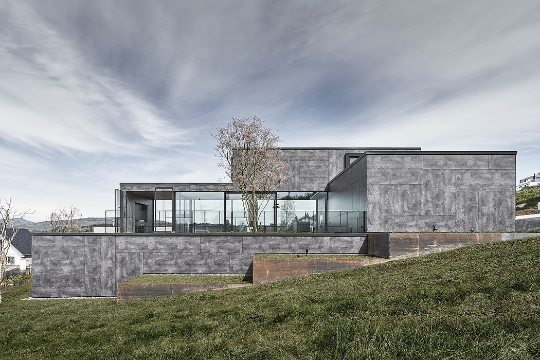 A modern, minimalist concrete structure with expansive glass walls and a lone tree.