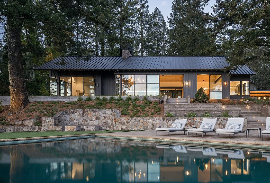 A modern, single-story home with a slanted metal roof, expansive windows, and a stone patio.