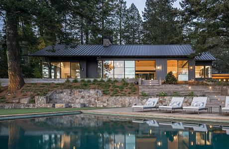 A modern, single-story home with a slanted metal roof, expansive windows, and a stone patio.