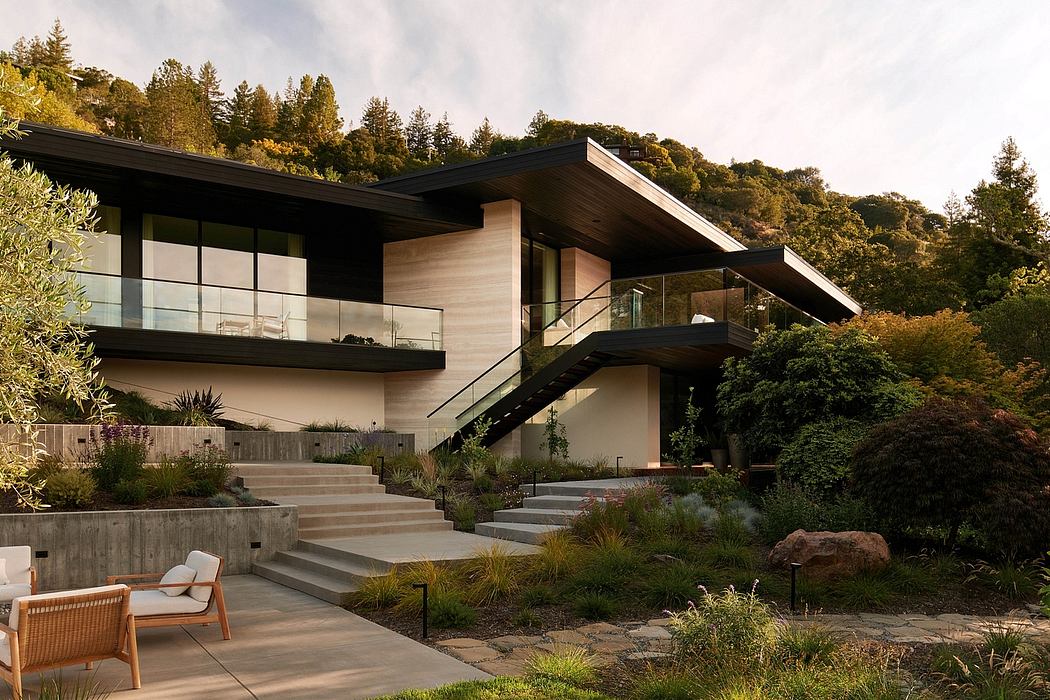 A modern, glass-walled house nestled among lush landscaping and towering trees.