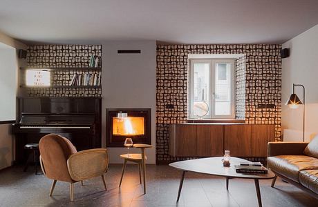 Cozy living room with wood-paneled walls, fireplace, piano, and mid-century modern furniture.