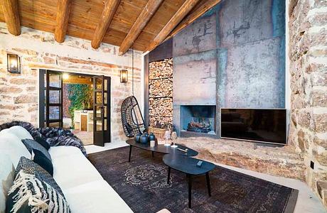 Rustic, cozy living room with exposed stone walls, wood beam ceiling, and modern furnishings.