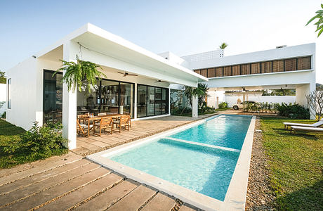 Modern, minimalist house with open floor plan, rectangular pool, and lush landscaping.