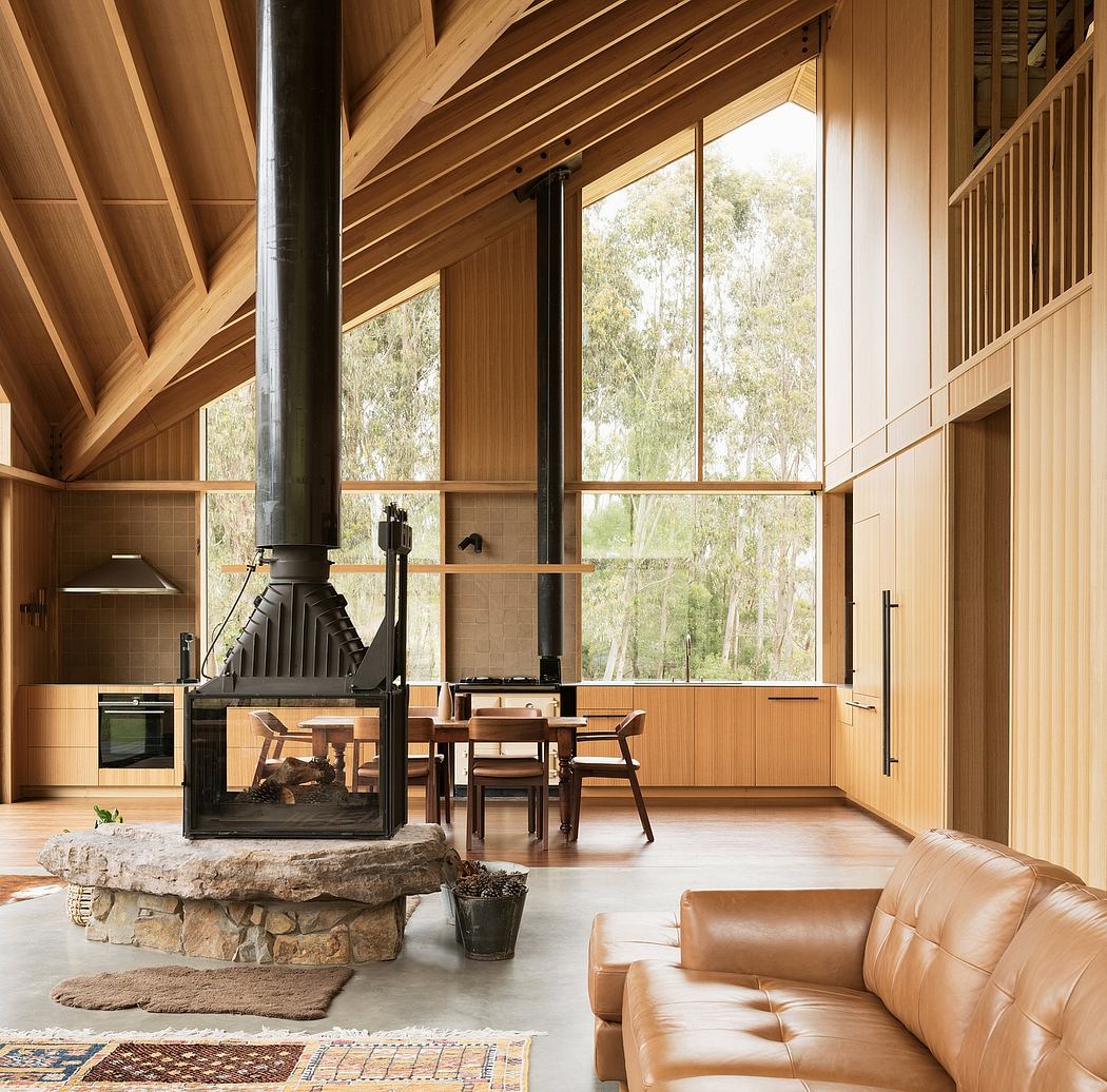 A cozy wooden cabin interior with a large fireplace, dining area, and panoramic forest views.