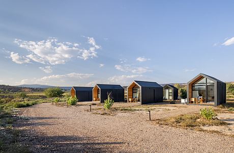 A collection of modern, minimalist cabins with dark exterior cladding and solar panels.