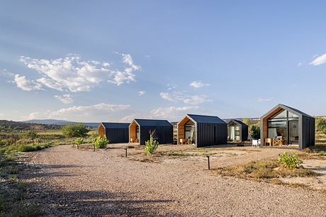 A collection of modern, minimalist cabins with dark exterior cladding and solar panels.