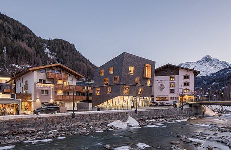 Modern, alpine-inspired architecture with wooden accents, set against snowy mountains.