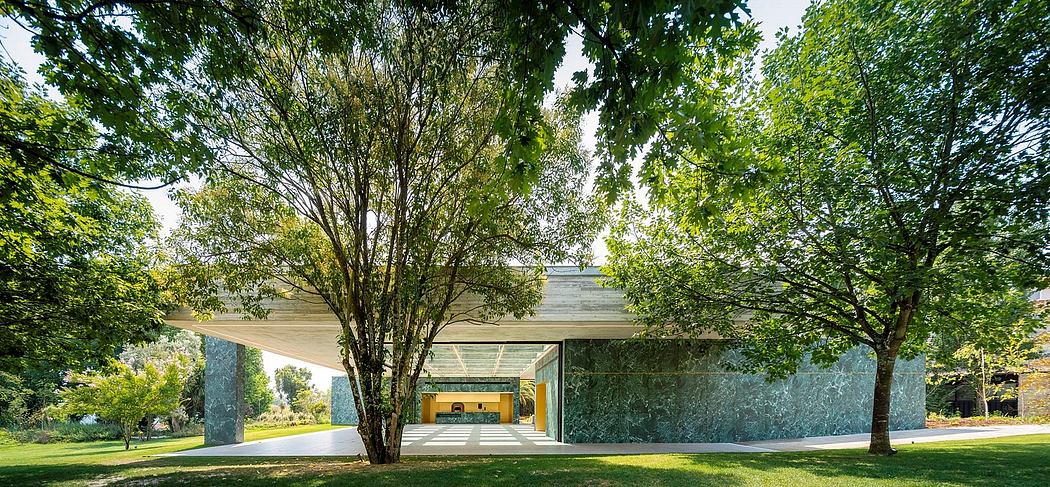 A modern glass and concrete structure surrounded by lush greenery and trees.