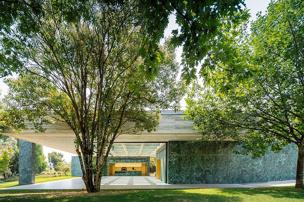A modern glass and concrete structure surrounded by lush greenery and trees.