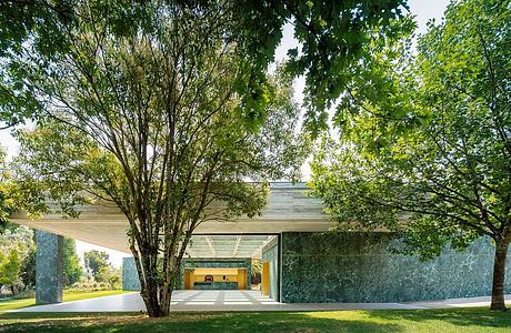 A modern glass and concrete structure surrounded by lush greenery and trees.