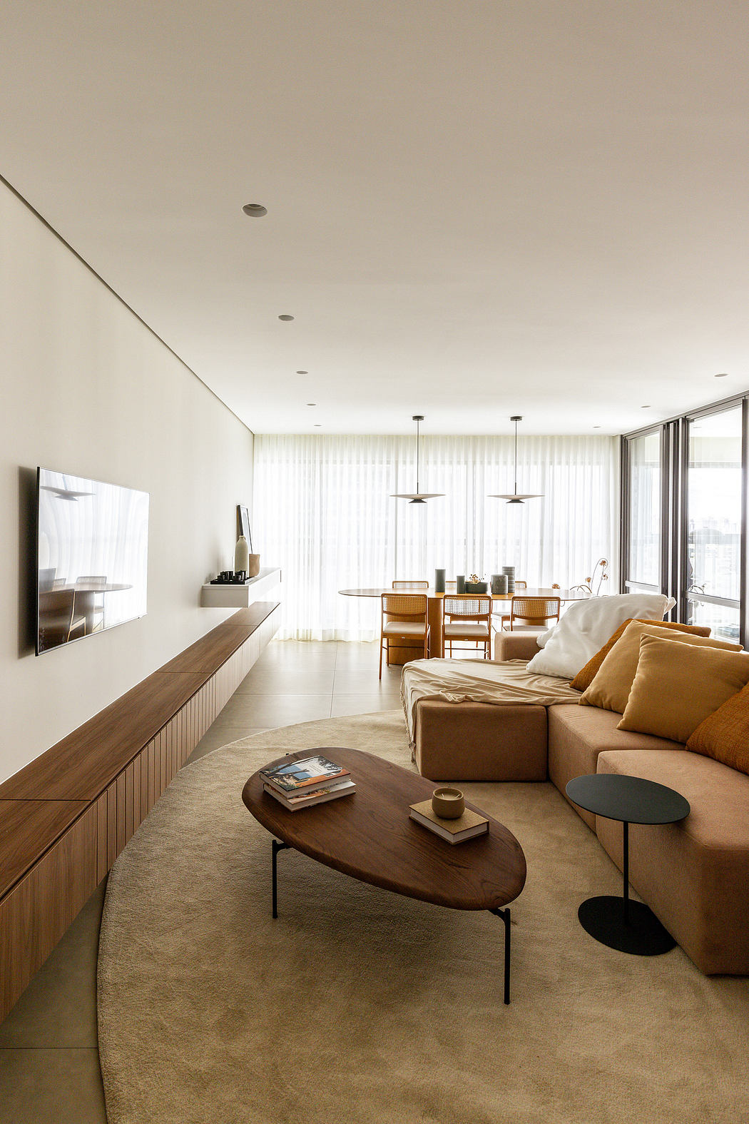 Minimalist living room with wood furniture, neutral tones, and large windows providing ample natural light.