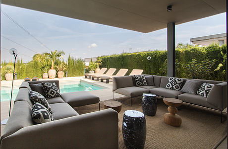 Sleek, modern outdoor living space with L-shaped couch, coffee tables, and pool.