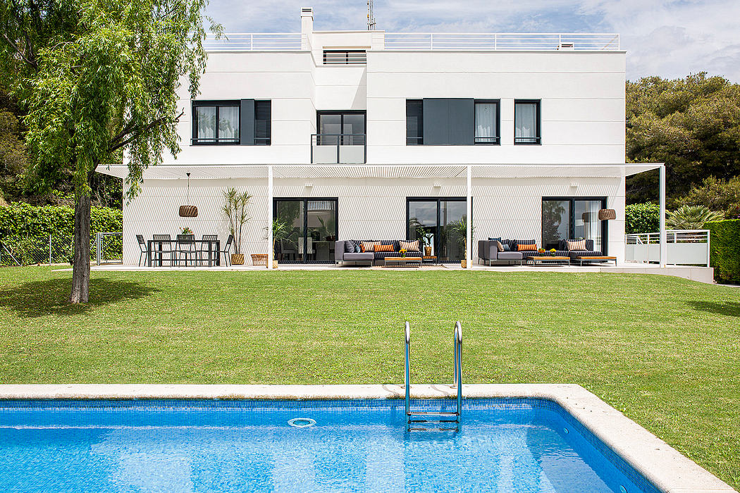 Modern white villa with pool, outdoor lounge, and lush green surroundings.