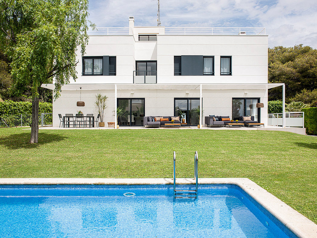 Modern white villa with pool, outdoor lounge, and lush green surroundings.