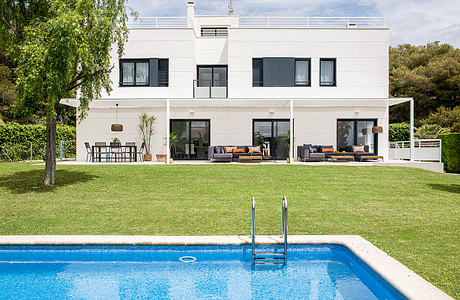 Modern white villa with pool, outdoor lounge, and lush green surroundings.