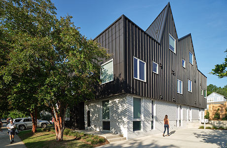 Modern angular building with metal facade, large windows, and landscaped surroundings.