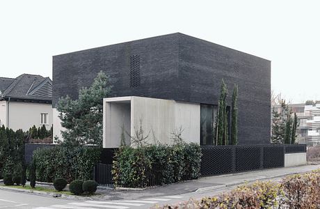 Striking modern building with dark brick exterior, minimal design elements, and surrounding greenery.