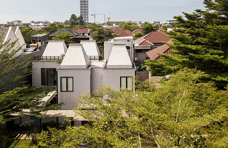 Modern townhouses with red tile roofs and large windows nestled in lush greenery.