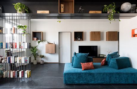 Minimalist living room with blue velvet sofa, shelves, and potted plants.