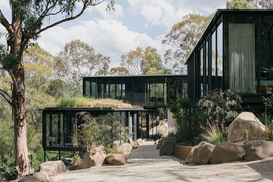 Modern glass and steel home nestled in lush bushland setting with rock formations.