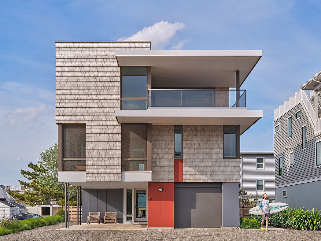 A modern, two-story house with shingle siding, glass balconies, and a vibrant red door.
