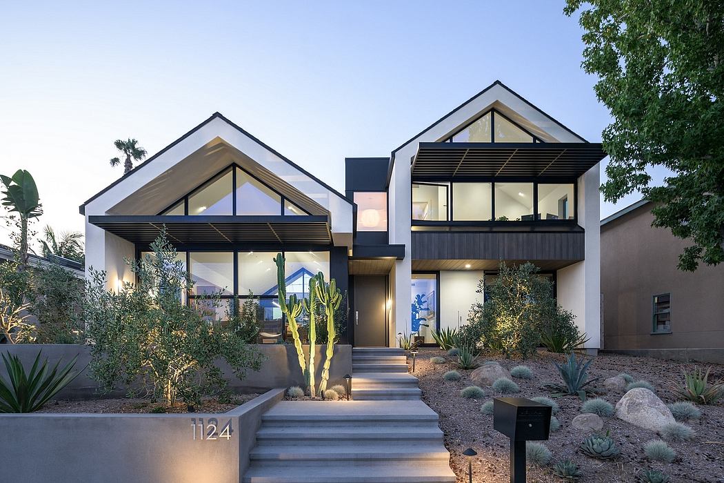 Modern two-story home with peaked roofs, large windows, and lush desert landscaping.