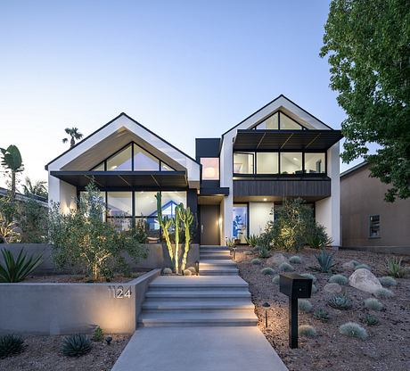 Modern two-story home with peaked roofs, large windows, and lush desert landscaping.