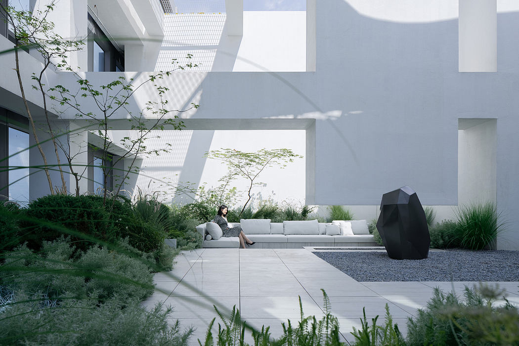 A modern, minimalist courtyard with lush greenery, concrete seating, and geometric sculptures.