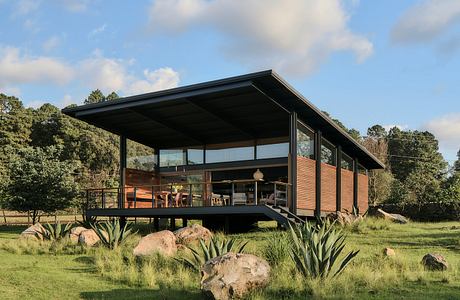 A modern, elevated wooden house with large windows and a spacious deck in a natural setting.