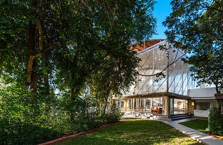 A modern building with large windows and a wooden exterior, surrounded by lush greenery.