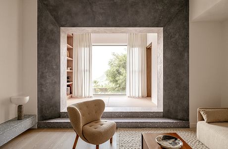 A minimalist living room with a large window, wood shelves, and a plush beige armchair.