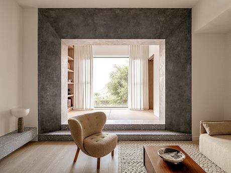 A minimalist living room with a large window, wood shelves, and a plush beige armchair.