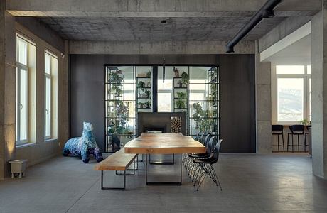 Industrial-style dining area with wooden table, bench, and plants in concrete space.