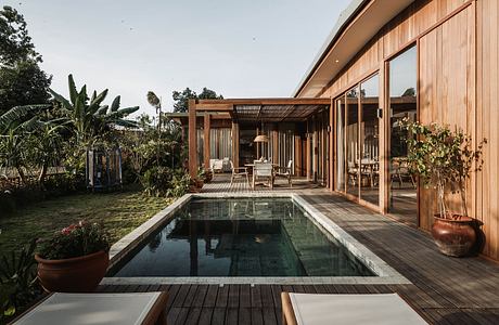 Rustic wooden house with covered patio, swimming pool, and lush tropical landscape.