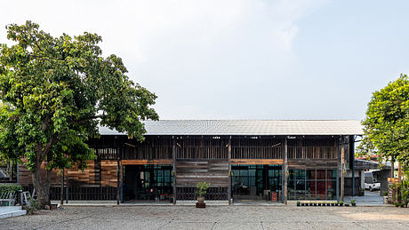 A rustic wooden structure with an expansive covered porch, surrounded by lush greenery.