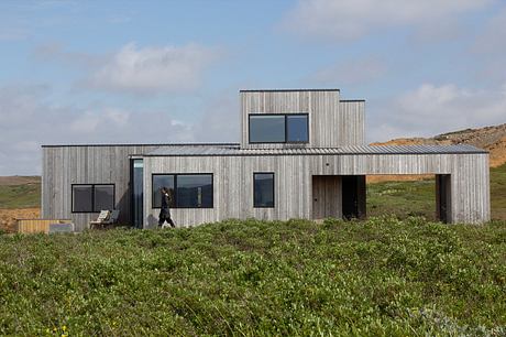 A modern, two-story structure with a metal facade and large windows, nestled in a grassy landscape.