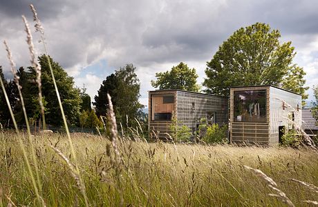 Rustic cabins nestled among lush greenery and tall grasses, reflecting a serene outdoor setting.