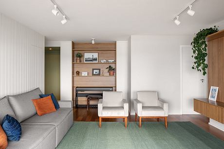 A cozy modern living room with a gray sofa, white armchairs, and a built-in wooden shelving unit.