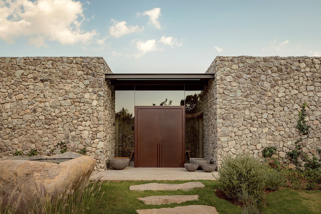 A rustic stone entryway with a modern wooden doorway, surrounded by lush landscaping.